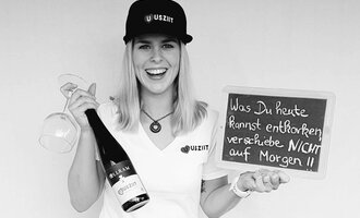 Eine fröhliche Frau hält ein Glas und eine Flasche Sekt in der Hand. Sie steht neben einer Tafel mit der Aufschrift: "Was Du heute kannst entfernen, verschiebe NICHT auf Morgen!!". | © Uusziit | Chantal Kessler