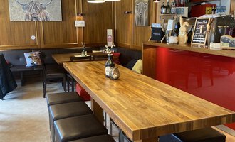 Eine moderne Bar mit einem langen Holztisch und stilvollen Hochstühlen. Die Wände sind in warmen Holz- und Rottönen gehalten, was eine gemütliche Atmosphäre schafft. | © Uusziit | Chantal Kessler