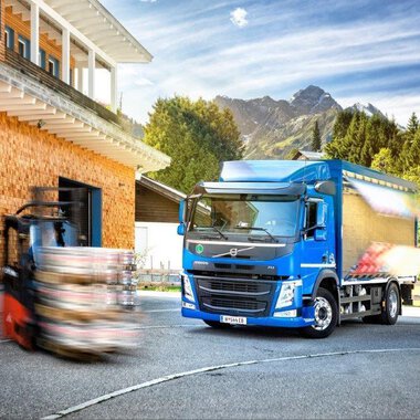 A blue truck is parked in front of a wooden building with the sign "Walser." In the background, there are mountains and a forklift visible. | © NUFA | Stefan Kothner