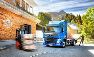 A blue truck is parked in front of a wooden building with the sign "Walser." In the background, there are mountains and a forklift visible. | © NUFA | Stefan Kothner