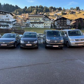 Two taxis are standing in front of a residential building. The black taxi and the white station wagon taxi are ready for passengers. | © Walser Taxi | Josef Düringer