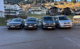 Two taxis are standing in front of a residential building. The black taxi and the white station wagon taxi are ready for passengers. | © Walser Taxi | Josef Düringer