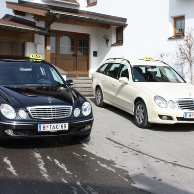 Zwei Taxis stehen vor einem Wohnhaus. Das schwarze Taxi und das weiße Kombi-Taxi sind bereit für Fahrgäste. | © Taxi Beranek | Elmar Beranek