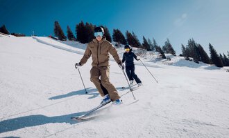 Zwei Skifahrer fahren die Piste hinunter. Der Himmel ist klar und die Umgebung ist schneebedeckt. | © Skischule Jörihalde Kleinwalsertal | Ole Zumpolle