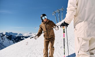 Ein Skifahrer mit einer braunen Skijacke steht auf einem schneebedeckten Hang. Im Hintergrund sind verschneite Berge und ein blauer Himmel zu sehen. | © Skischule Jörihalde Kleinwalsertal | Oliver Farys