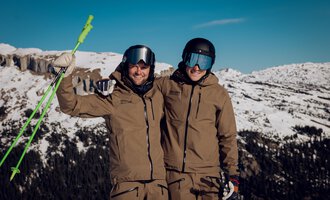 Zwei Skifahrer posieren fröhlich in den Bergen. Sie tragen Skikleidung und stehen vor einer schneebedeckten Landschaft. | © Skischule Jörihalde Kleinwalsertal | Ole Zumpolle
