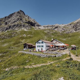 © Widdersteinhütte | Vanessa Wüstner A picturesque mountain restaurant surrounded by green meadows and mountains. The clear sky provides a beautiful backdrop for the place. | © Widdersteinhütte | Vanessa Wüstner