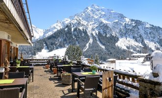 A terrace with tables and chairs, surrounded by snow-capped mountains. The clear blue sky creates an inviting atmosphere. | © Wirtshaus Hoheneck | Klaus Ruland
