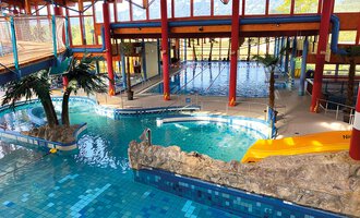 Ein farbenfrohes Hallenbad mit verschiedenen Becken und einer tropischen Atmosphäre. Palmen und Felsen schaffen ein entspannendes Ambiente. | © WONNEMAR