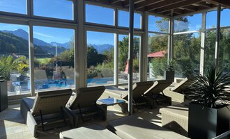 Ein ruhiger Wellnessbereich mit Liegen und großen Fenstern. Im Hintergrund sind Berge und ein Pool sichtbar. | © WONNEMAR Sonthofen | Julia Sondergelt
