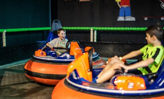 Zwei Kinder fahren mit elektronischen Bumper Cars in einer Sporthalle. Eines der Kinder hat einen Ausdruck voller Freude und Aufregung im Gesicht. | © Wonniland Sonthofen | interSPA Gruppe