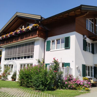 Ein charmantes Haus mit bunten Blumen vor dem Fenster. Der Himmel ist klar und die Architektur ist traditionell.