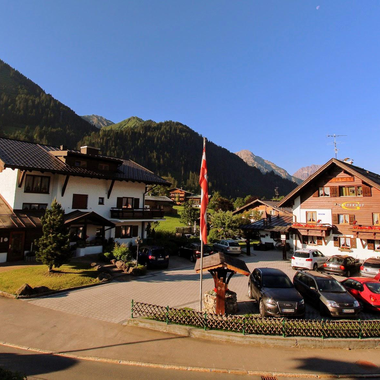 Ein malerisches Gebäude in einer Berglandschaft mit klar blauem Himmel. Autos parken auf dem Platz vor den Häusern.