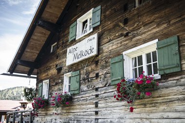 Holzhaus mit grünen Fensterläden und Blumenfensterkästen, Beschilderung 'Alpe Melköde', im Schwarzwald | © Kleinwalsertal Tourismus eGen • Fotograf: Andre Tappe