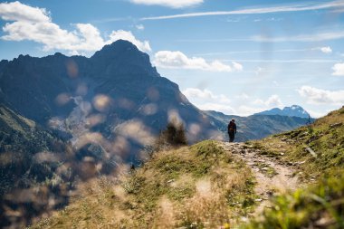 Ein Wanderer geht auf einem Pfad in den Bergen im Schwarzwald bei schönem Wetter, umgeben von grünem Gras und Bergen im Hintergrund. | © Kleinwalsertal Tourismus eGen • Fotograf: Andre Tappe