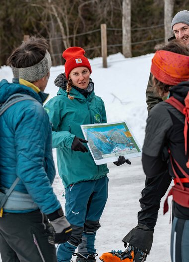 Gruppe von Wanderern im Schnee im Gespräch, eine Person hält eine Karte, draußen im Winterwald | © Kleinwalsertal Tourismus eGen • Fotograf: Basti Heckl