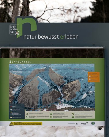 Informationsschild im Winter in einem Naturschutzgebiet, mit einer Karte der Berge und Texten zu Umwelt | © Kleinwalsertal Tourismus eGen • Fotograf: Basti Heckl