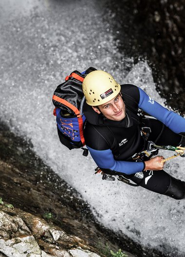 Abenteurer beim Klettern und Abseilen in einer Wasserfall-Umgebung, ausgesetzt an einem Seil, mit Helm und voller Ausrüstung. | © Kleinwalsertal Tourismus eGen • Fotograf: Dominik Berchtold