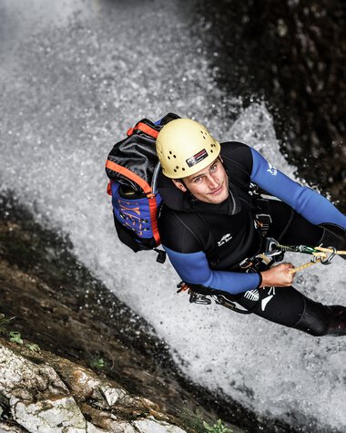 Abenteurer beim Klettern und Abseilen in einer Wasserfall-Umgebung, ausgesetzt an einem Seil, mit Helm und voller Ausrüstung. | © Kleinwalsertal Tourismus eGen • Fotograf: Dominik Berchtold