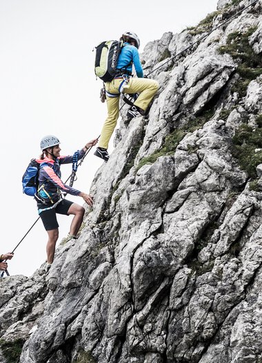 Menschen klettern an einem steilen Felsen im Berg, alle mit Kletterausrüstung und Helmen. | © Kleinwalsertal Tourismus eGen • Fotograf: Dominik Berchtold
