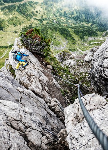 Kletterer beim Klettersteig in den Bergen, Blick nach oben auf die Felswand, durch die ein Seil führt. | © Kleinwalsertal Tourismus eGen • Fotograf: Dominik Berchtold