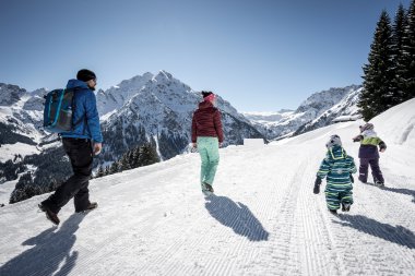 Familie beim winterlichen Wandern in den Bergen, mit schneebedeckten Gipfeln im Hintergrund. | © Kleinwalsertal Tourismus eGen • Fotograf: Dominik Berchtold