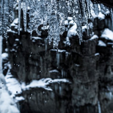 Eiszapfen hängen von einem Dach über einem winterlichen Fluss in der Breitachklamm, mit Schneeschauern im Hintergrund. | © Kleinwalsertal Tourismus eGen • Fotograf: Dominik Berchtold