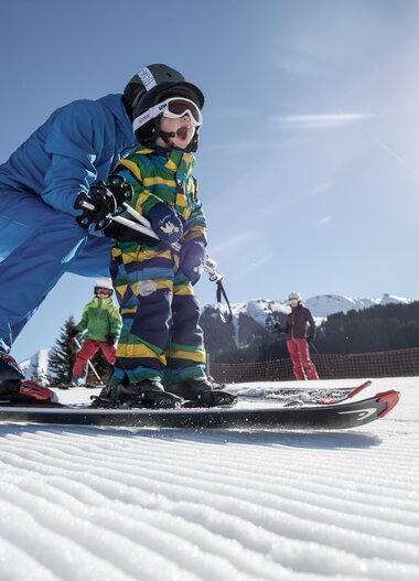 Familie beim Skifahren auf einem sonnigen Wintertag in den Bergen, Kinder lernen das Skifahren. | © Kleinwalsertal Tourismus eGen • Fotograf: Dominik Berchtold