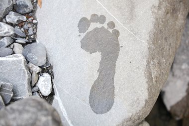 Eine nahe Aufnahme eines Steins mit einem natürlichen Fußabdruck, umgeben von kleinen Steinen und Kies. | © Kleinwalsertal Tourismus eGen • Fotograf: Frank Drechsel