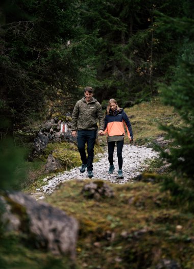 Ein Paar wandert Hand in Hand durch einen bewaldeten Pfad in der Natur bei Tageslicht. | © Kleinwalsertal Tourismus eGen • Fotograf: Hannah Bichay
