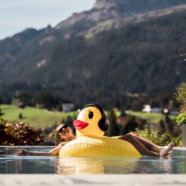 Ein Mädchen entspannen auf einer Schwimmreifen in Form eines Enten im Pool mit Berglandschaft im Hintergrund.