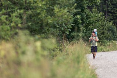 Familie wandert auf einem Waldweg im Wildental, mit viel Grün und Bäumen im Hintergrund. | © Kleinwalsertal Tourismus eGen • Fotograf: Oliver Farys