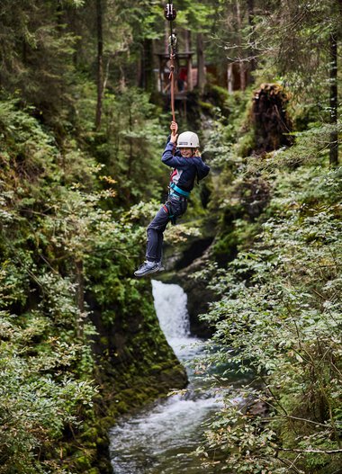 Junge Person beim Ziplining über einen Bach in einem grünen Wald im Kleinwalsertal. | © Kleinwalsertal Tourismus eGen • Fotograf: Oliver Farys