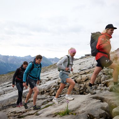 Vier hikers steigen eine felsige Steigung im Bergland bei Sonnenaufgang im Kleinwalsertal auf. | © Kleinwalsertal Tourismus eGen • Fotograf: Oliver Farys