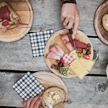 Frühstückstisch mit verschiedenen Brotsorten, Käse, Aufschnitt und Getränken auf einer Holztafel bei einer Wanderung im Kleinwalsertal. | © Kleinwalsertal Tourismus eGen • Fotograf: Oliver Farys