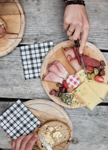 Frühstückstisch mit verschiedenen Brotsorten, Käse, Aufschnitt und Getränken auf einer Holztafel bei einer Wanderung im Kleinwalsertal. | © Kleinwalsertal Tourismus eGen • Fotograf: Oliver Farys