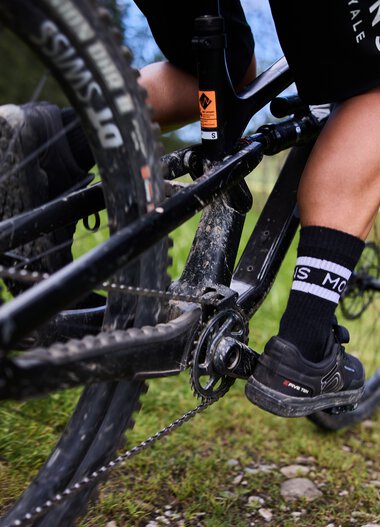 Nahaufnahme eines Mountainbikers, der auf einem Singletrail im Kleinwalsertal fährt, mit Fokus auf die Pedale und die Kette. | © Kleinwalsertal Tourismus eGen • Fotograf: Oliver Farys
