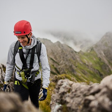 Abenteuerliche Klettertour auf einem Berg mit einem lächelnden Kletterer in Kletterausrüstung und Helm. | © Kleinwalsertal Tourismus eGen • Fotograf: Oliver Farys