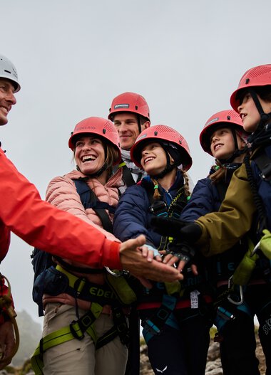 Gruppenfoto bei einem Klettersteig-Abenteuer in den Bergen, mit einer Bergführer-Person, die die Gruppe begrüßt oder willkommen heißt.
