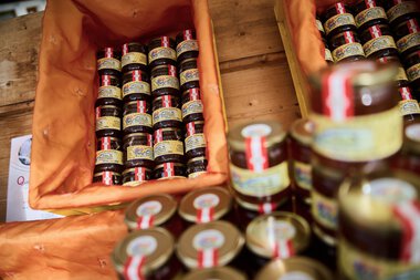 Mehrere Gläser mit Marmelade stehen in einer orangefarbenen Kiste auf einem Markt. | © Kleinwalsertal Tourismus eGen • Fotograf: Oliver Farys