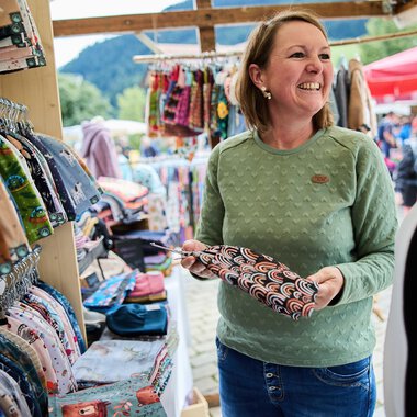 Frau verkauft handgefertigte Stoffe an einem Markt im Kleinwalsertal bei sommerlichem Wetter. | © Kleinwalsertal Tourismus eGen • Fotograf: Oliver Farys
