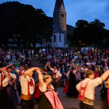 Bilder von einer Trachtengruppe beim Alpenzauber Festival im Kleinwalsertal mit tanzenden Jugendlichen im traditionellen Gewand während der Dämmerung. | © Kleinwalsertal Tourismus eGen • Fotograf: Oliver Farys