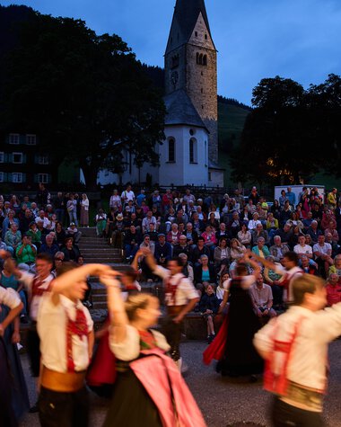 Bilder von einer Trachtengruppe beim Alpenzauber Festival im Kleinwalsertal mit tanzenden Jugendlichen im traditionellen Gewand während der Dämmerung. | © Kleinwalsertal Tourismus eGen • Fotograf: Oliver Farys