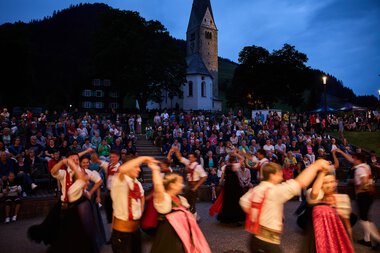Bilder von einer Trachtengruppe beim Alpenzauber Festival im Kleinwalsertal mit tanzenden Jugendlichen im traditionellen Gewand während der Dämmerung. | © Kleinwalsertal Tourismus eGen • Fotograf: Oliver Farys