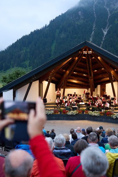 Öffentliches Konzert auf einer offenen Bühne in einem Bergort mit vielen Zuschauern, die das Sommer-Open-Air genießen. | © Kleinwalsertal Tourismus eGen • Fotograf: Oliver Farys