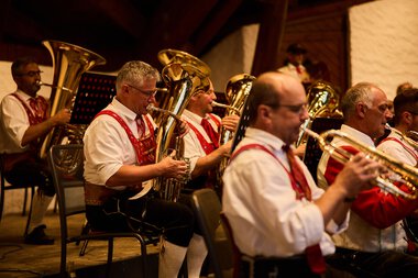 Blasmusikkapelle in traditionellen Trachten spielt während eines Konzerts in einem Holzraum. | © Kleinwalsertal Tourismus eGen • Fotograf: Oliver Farys