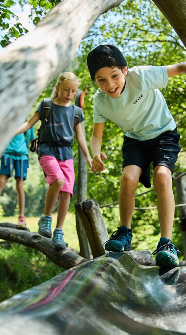 Kinder spielen auf einem Holzsteg im Wald, lachen und erkunden die Natur im Kleinwalsertal. | © Kleinwalsertal Tourismus eGen • Fotograf: Oliver Farys