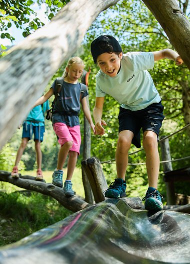 Kinder spielen auf einem Holzsteg im Wald, lachen und erkunden die Natur im Kleinwalsertal. | © Kleinwalsertal Tourismus eGen • Fotograf: Oliver Farys