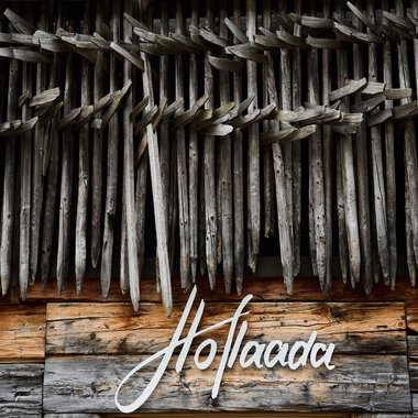 Blick auf eine Holzwand mit einer dekorativen Struktur aus Holzspänen, darunter eine Holztafel mit dem Schriftzug 'Hoflaada'. | ©  Kleinwalsertal Tourismus eGen • Fotograf: Oliver Farys