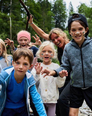 Fünf fröhliche Kinder beim Sommerabenteuer im Freien, lächelnd und spielend an einem Fluss, umgeben von grüner Natur. | © Kleinwalsertal Tourismus eGen • Fotograf: Oliver Farys